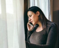 Грустная девушка разговаривает по телефону у окна